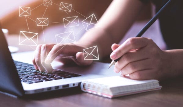 hands typing on laptop keyboard and writing notes in notebook