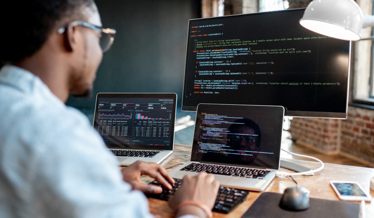 programmer working on two laptop and three screens